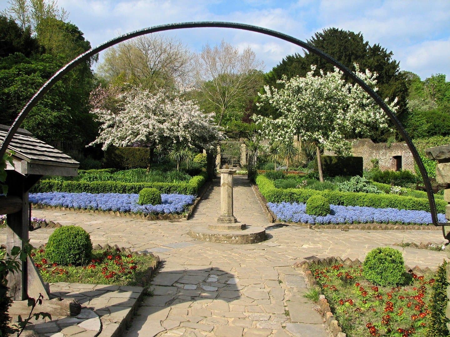 The Rookery formal gardens at Streatham Common — ornamental stone arch, blue muscari flowers, box hedging and cherry blossom trees in spring